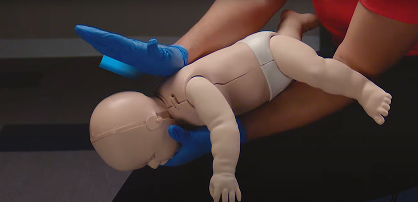 Infant mannequin choking-response training with an instructor demonstrating the Heimlich maneuver